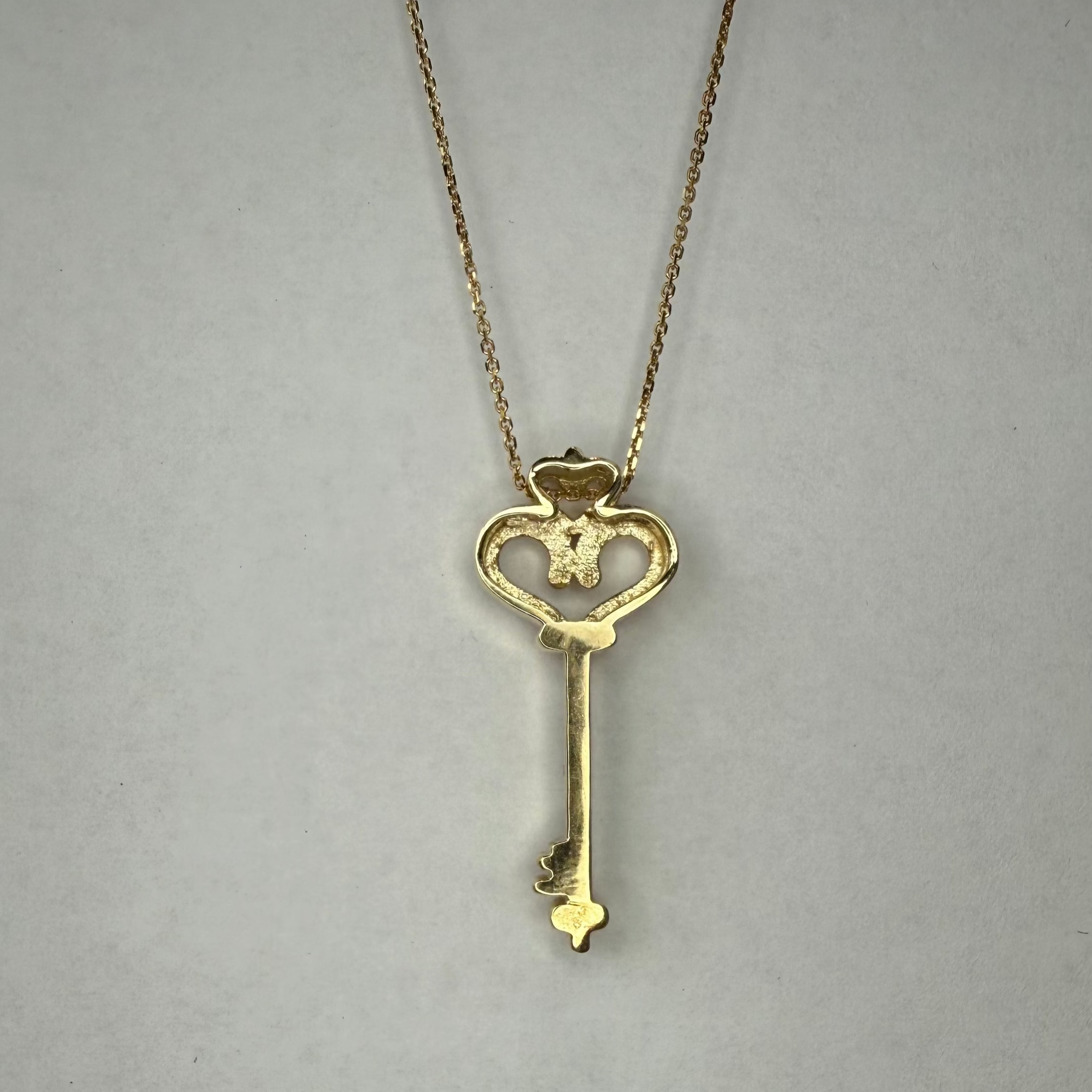 Gold key-shaped pendant necklace on a plain background