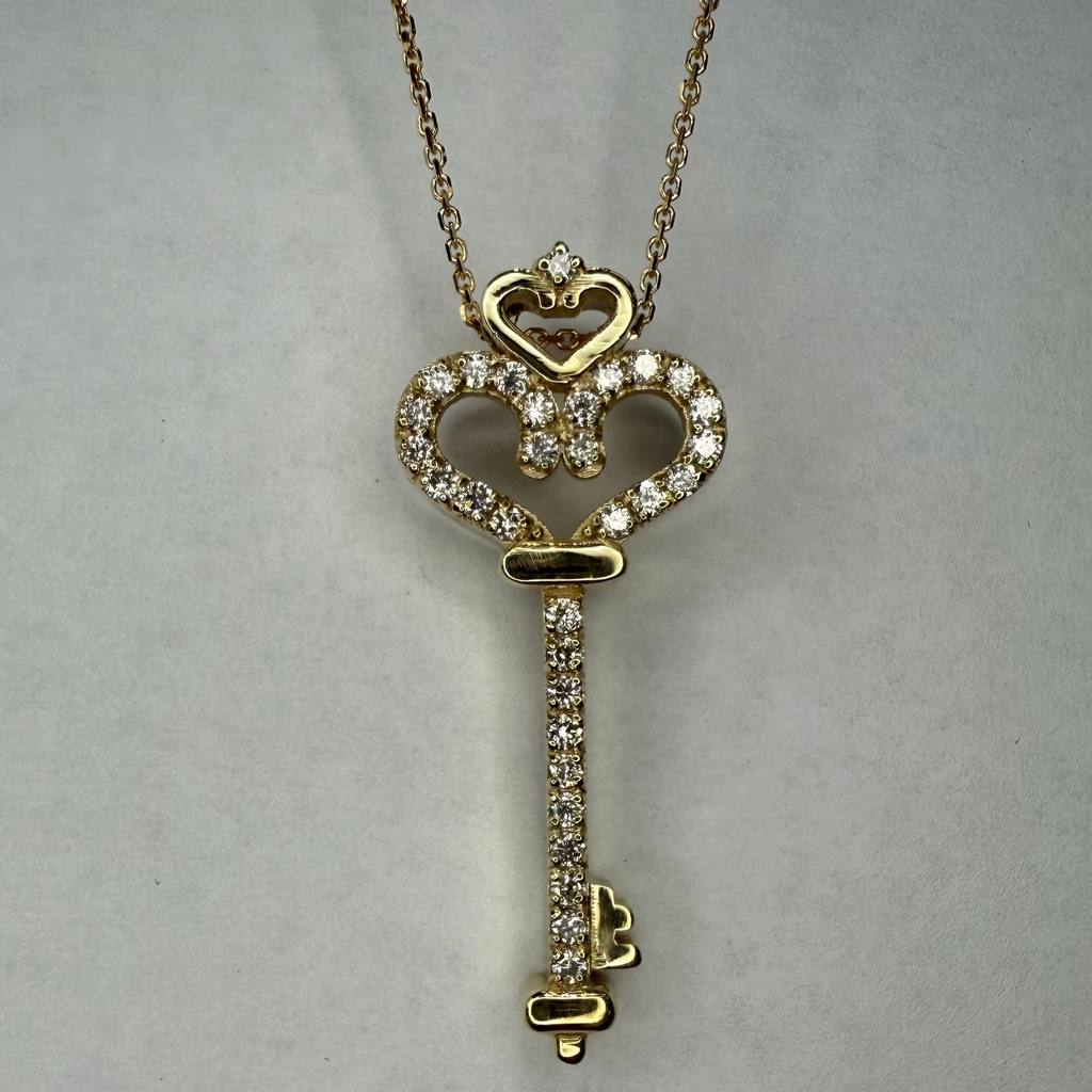 Gold key-shaped pendant necklace on a gray background